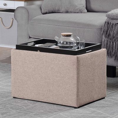 Black serving tray with glass pitcher and cups on beige storage ottoman in modern living room, blending functionality with elegant decor.