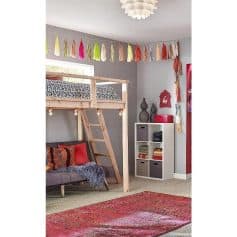Vibrant tassel garland hanging in a cozy kids' bedroom with a loft bed, decorative cushions, and storage cubes, perfect for playful nursery or kids’ room decor.