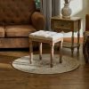 Vintage-style wooden vanity stool with tufted white cushion, placed on a decorative rug in a cozy, well-decorated living room. Perfect for bedroom or dressing room decor.