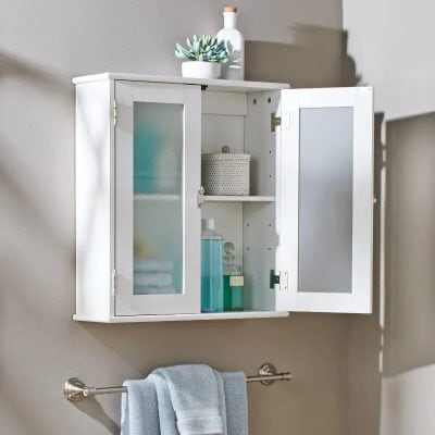A white bathroom wall cabinet with frosted glass doors, storing toiletries, skincare, and decorative items, ideal for organizing your bathroom essentials efficiently.