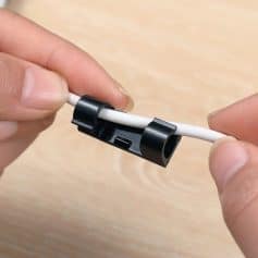 A black cable clip secures a white optical fiber cable, preventing tangling and damage. Perfect for organizing electronic cables at optometry clinics and optical stores for a tidy workspace.