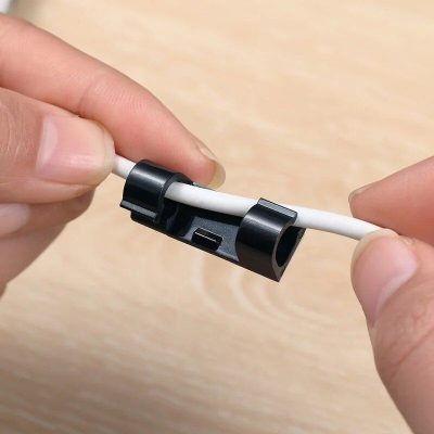 A black cable clip secures a white optical fiber cable, preventing tangling and damage. Perfect for organizing electronic cables at optometry clinics and optical stores for a tidy workspace.