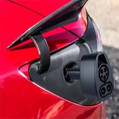 ALT: Close-up of Tesla EV charging port with charging cable inserted on a red electric car, showcasing fast-charging technology and modern design for eco-friendly transportation.