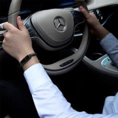 Close-up of a person holding a Mercedes-Benz steering wheel inside a luxury car, showcasing premium interior and driving experience.