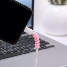 Stylish pink spiral cable organizer connecting phone to laptop charger for desk setup.
