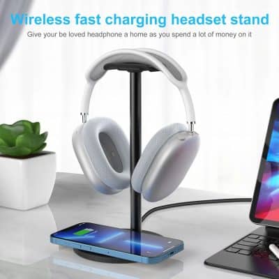 Wireless fast charging headphone stand on a sleek desk setup with a smartphone, laptop, and decorative plant.