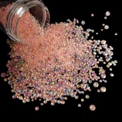 Assorted pink and white pearl beads spilling from a container on a black background, ideal for jewelry making and nail art supplies.