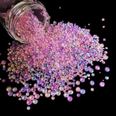 Vibrant pink rhinestones spilled from a jar, ideal for eye makeup, nail art, and beauty enhancements, showcasing high-quality cosmetic rhinestones for stylish eye decorations.