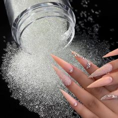 Close-up of a small jar spilling rhinestones onto a black surface, with a hand showcasing long, decorated acrylic nails adorned with rhinestones for a glamorous look.