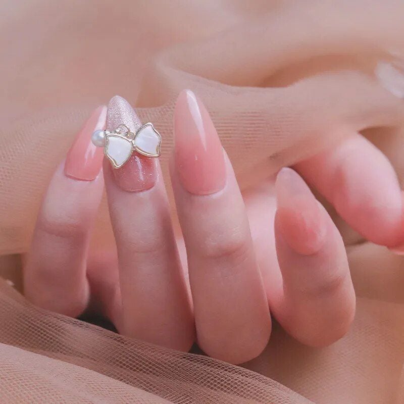 Delicate pink and white gel nails with a cute bow ring, promoting stylish nail art and accessories. Perfect for enhancing your look with luxury nail designs and jewelry.