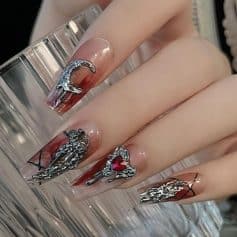 Intricate nail art featuring metallic silver embellishments and a heart-shaped red gemstone on a stylish, glossy finish. Perfect for showcasing luxury nail trends and high-end manicure styles.
