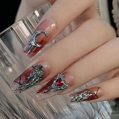 Intricate nail art featuring metallic silver embellishments and a heart-shaped red gemstone on a stylish, glossy finish. Perfect for showcasing luxury nail trends and high-end manicure styles.