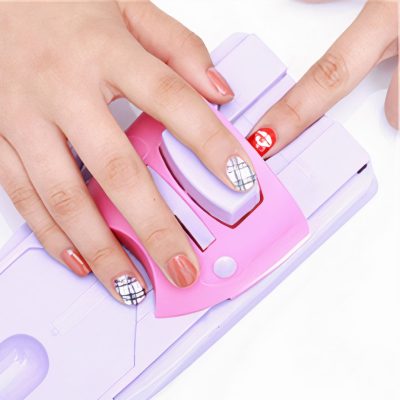 Close-up of hands with stylish manicured nails, showcasing trendy nail art designs on a nail stamping device for a modern manicure look.