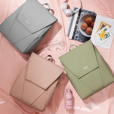 Contemporary designer handbags in pastel tones showcased with magazines, headphones, and snacks on a soft pink background, highlighting trendy, functional, and fashionable options.