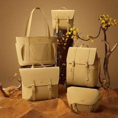 Light-colored handbags and backpacks with minimalistic design arranged on wooden stumps and surrounded by flowering branches, highlighting fashion-forward, high-quality accessories for women.