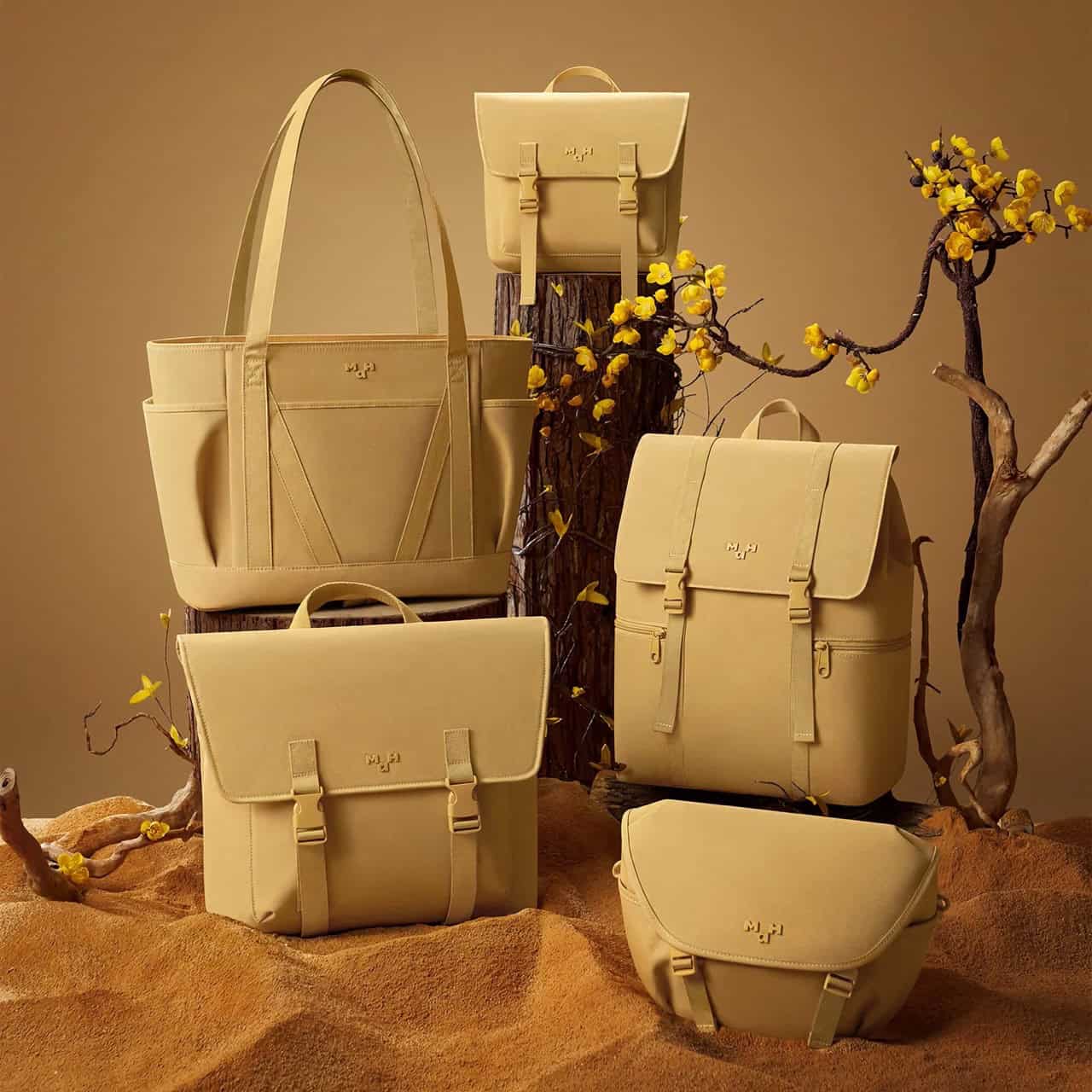 Light-colored handbags and backpacks with minimalistic design arranged on wooden stumps and surrounded by flowering branches, highlighting fashion-forward, high-quality accessories for women.