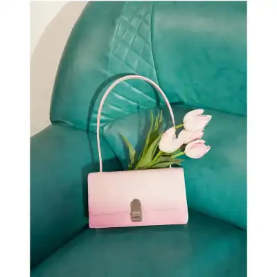 Pink handbag with silver clasp placed on teal sofa, accompanied by a bouquet of white tulips. Perfect for fashion-forward accessories and elegant style at Monalisa Store.