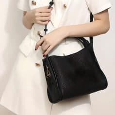 Close-up of a woman's hand holding a stethoscope, with a black handbag and a white outfit, emphasizing style and sophistication in optometry service settings.
