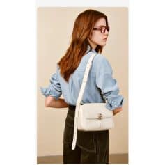 Elegant white handbag layered over a casual light blue shirt and black jeans, perfect for fashion-forward woman.