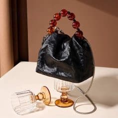 Stylish black leather purse with a unique amber bead handle, perfect for trendy accessories and fashion-forward looks. Compact design ideal for evening outings and special events.
