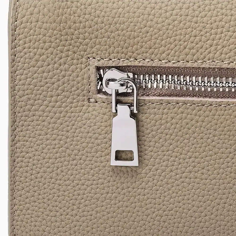 Close-up of a beige leather bag featuring a sleek silver zipper and locking system, emphasizing style and security for accessories or personal items.