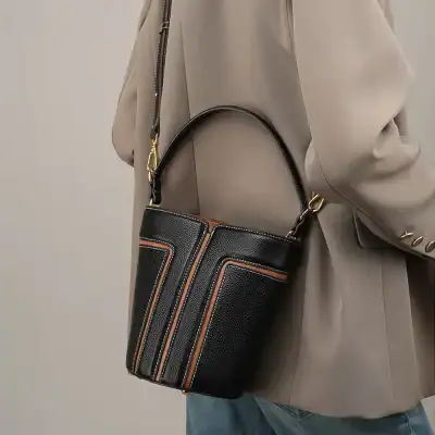 Stylish black handbag with orange and beige accents, perfect for fashion-conscious women, featuring a sleek textured finish and adjustable shoulder strap for versatile looks.