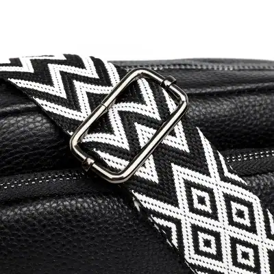 Zippered black leather handbag with a black and white geometric patterned strap, featuring a sleek metallic buckle, high-quality textured leather, perfect for fashionable everyday use.
