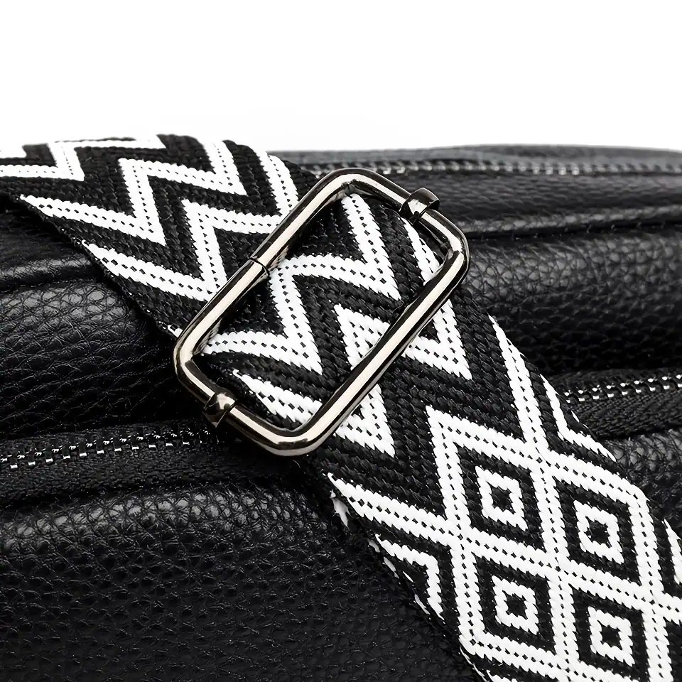 Zippered black leather handbag with a black and white geometric patterned strap, featuring a sleek metallic buckle, high-quality textured leather, perfect for fashionable everyday use.