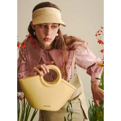 Stylish pastel yellow handbag with round handle, lightweight, and spacious, perfect for women seeking trendy accessories. Designed for a modern, chic look.