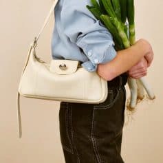 A chic white handbag worn by a person holding fresh green vegetables, showcasing stylish fashion accessories perfect for casual or sophisticated looks.