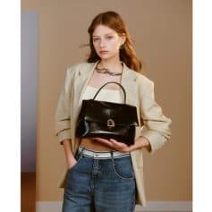 Elegant woman holding a stylish black handbag with a lock detail, dressed in trendy casual attire, emphasizing fashion and accessories for modern women.