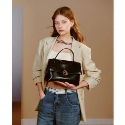 Elegant woman holding a stylish black handbag with a lock detail, dressed in trendy casual attire, emphasizing fashion and accessories for modern women.