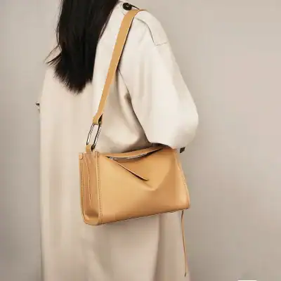 Stylish beige leather shoulder bag featured on woman wearing a cream-colored trench coat, perfect for professional or casual occasions, highlighting trendy women's accessories.