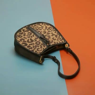 Leopard print handbag with black leather accents and adjustable strap, perfect for stylish outings.