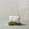 Luxurious white handbag with braided strap, placed on green moss and reflective surface, showcasing stylish designer accessories perfect for fashion and beauty enthusiasts.