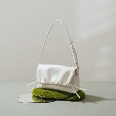 Luxurious white handbag with braided strap, placed on green moss and reflective surface, showcasing stylish designer accessories perfect for fashion and beauty enthusiasts.