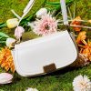 Stylish white handbag with gold accent, perfect for fashionable accessories, placed on a vibrant bouquet of tulips and lilies, ideal for trendy fashion statements.