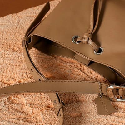Close-up of stylish beige handbag with silver accents on textured coral background.