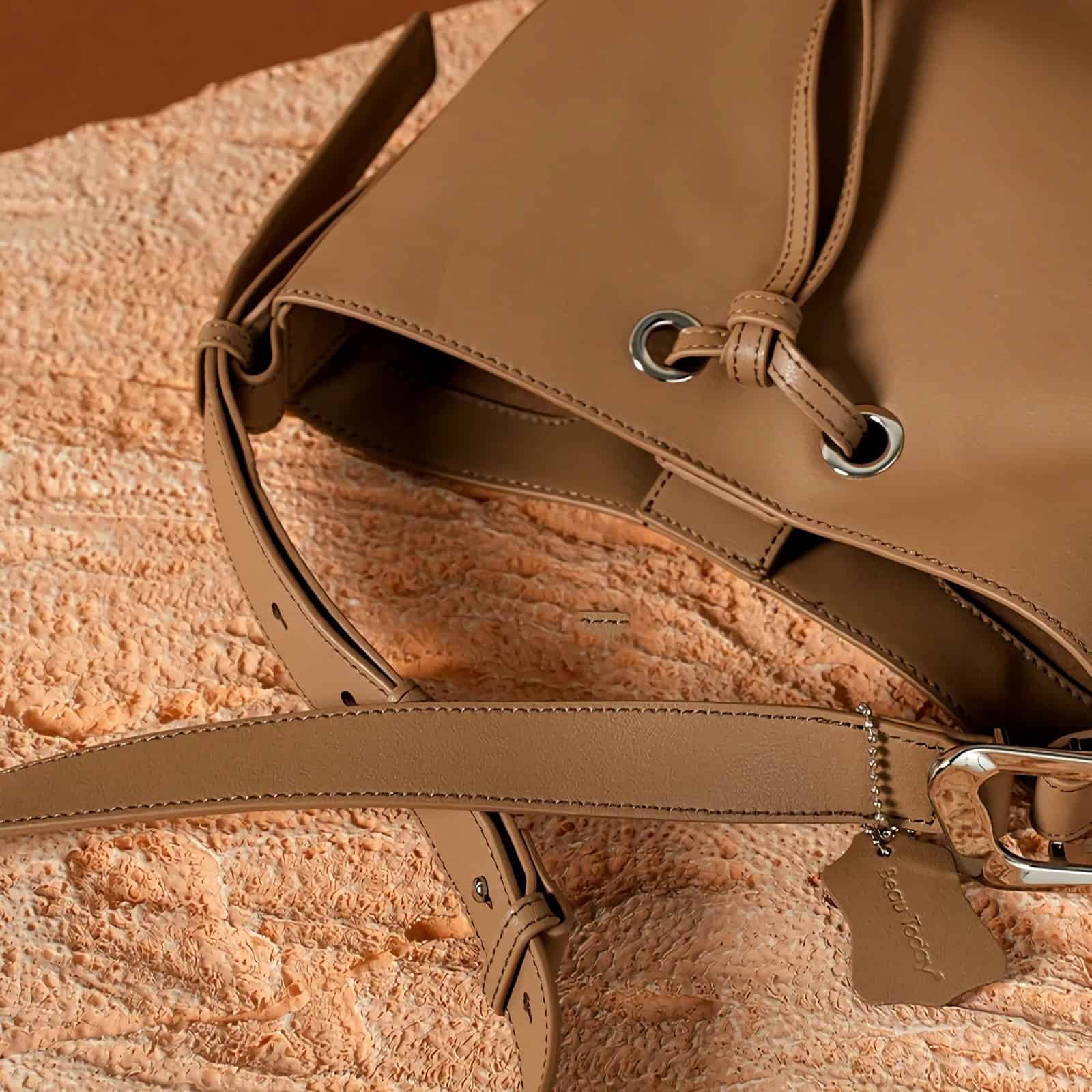 Close-up of stylish beige handbag with silver accents on textured coral background.