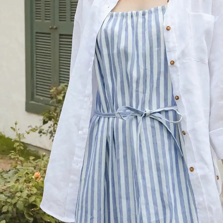 A stylish blue and white striped cotton dress featuring a tie waist detail, perfect for casual or summer wear, complemented by a white linen jacket for a chic layered look.