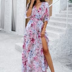 Beautiful woman wearing a floral maxi dress with a slit, accessorized with a wide-brim hat and jewelry, on a bright summer day, perfect for vacation or outdoor events.