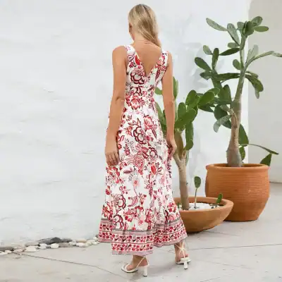 Woman wearing a white and red floral maxi dress with open back, standing outdoors with potted plants.