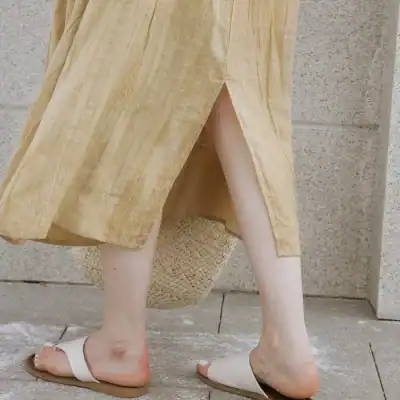 Comfortable women's casual wear featuring a beige skirt with a high slit paired with white slides, perfect for everyday outings.