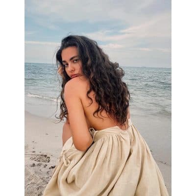 Close-up of a woman with curly hair sitting on a beach, showcasing stylish eyewear options available at Monalisa Store for optical needs.