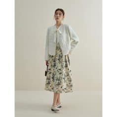 Stylish woman wearing a white cardigan with bow detail, paired with a floral-printed skirt, perfect for elegant daytime look.